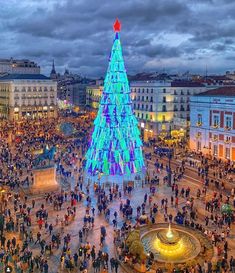 a large christmas tree is lit up in the middle of a square with people standing around it