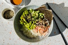 a bowl filled with rice and vegetables next to chopsticks on top of a table