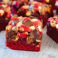 several pieces of red velvet cake with chocolate chips and nuts on top, sitting on a white surface