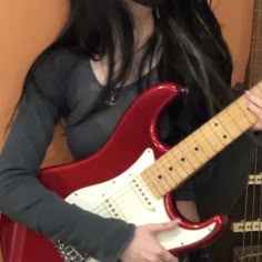 a woman with long black hair is holding a red and white guitar in her hands