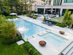 an aerial view of a pool surrounded by greenery and lawn furniture in front of a house