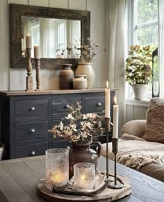 a table with candles and vases on it in front of a couch, mirror and window