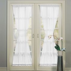 a vase with flowers in it sitting next to two large white curtains on a window sill