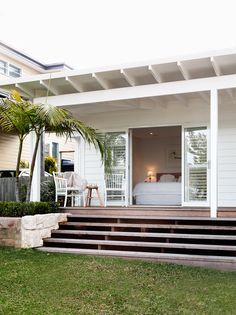 a white house with steps leading to the front door and patio area that has palm trees on both sides