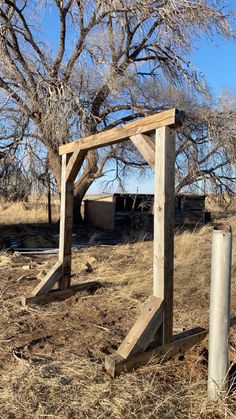 a wooden structure sitting in the middle of a dry grass field next to a tree