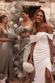 three bridesmaids standing in front of a floral backdrop with white flowers and greenery