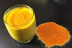 a glass filled with orange juice next to a pile of spices