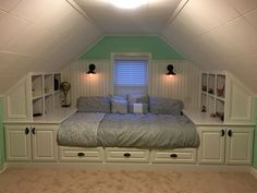 a bed sitting in the middle of a bedroom under a slanted ceiling with built - in bookshelves