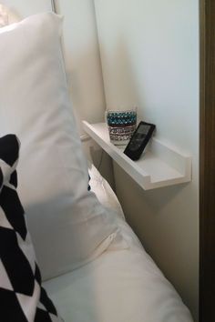 a cell phone sitting on top of a white shelf next to a bed with black and white pillows