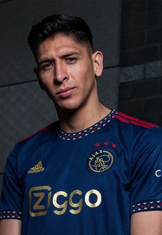 a soccer player poses for a photo in his blue uniform with gold lettering on it