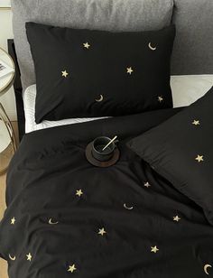 a bed with black sheets and gold stars on the pillowcase, next to a night stand