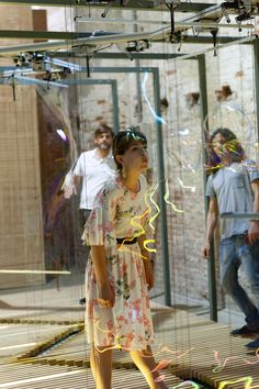 a woman standing in front of a glass wall with people looking at it and confetti falling from the ceiling