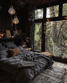 an unmade bed in front of a large window with lights hanging from the ceiling