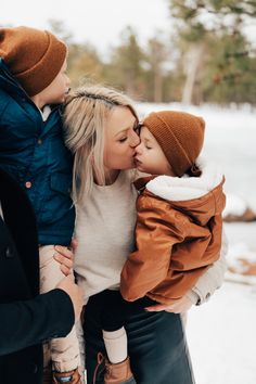 a mother and her two children are kissing in the snow with trees in the background