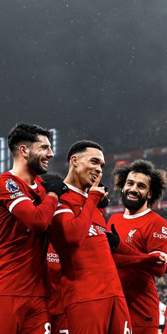 three men in red soccer uniforms are standing together and one man is holding his hand up to his mouth