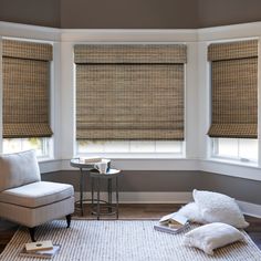 a living room with two large windows covered in bamboo blinds and white pillows on the floor