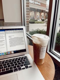 a laptop computer sitting on top of a wooden table next to a cup of coffee