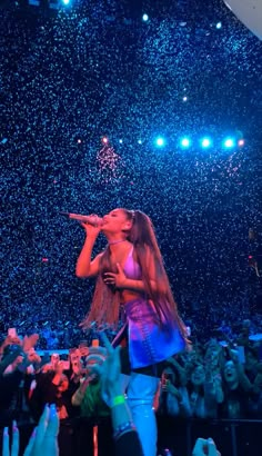 a woman standing on top of a stage with her hands in the air while singing