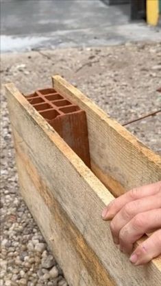 a person is holding something in their hand while standing next to a piece of wood