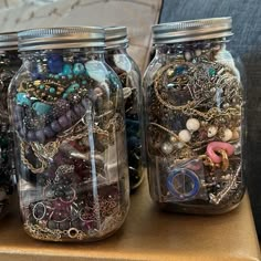 three mason jars filled with different types of beads and jewelry sitting on a table next to a couch