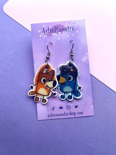 two cartoon characters are hanging from earrings on a piece of purple paper next to a white envelope