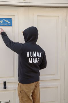 a person in a black hoodie pointing at a door with the words human made on it