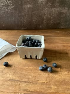 some blueberries are in a white bowl on a wooden table next to a napkin