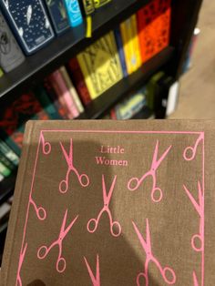 a little women book with pink scissors on it's cover in front of bookshelves