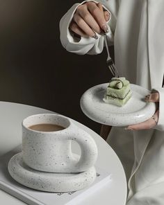 a woman holding a plate with some food on it and a cup of coffee in front of her