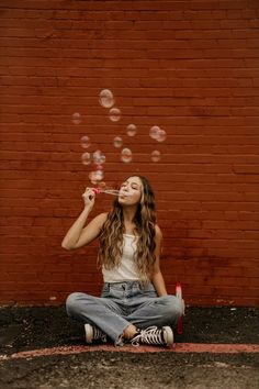 a young woman sitting on the ground blowing bubbles in front of her face while she sits down