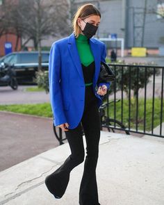 a woman wearing a face mask while walking down the street with her hand in her pocket