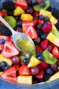 a bowl full of fresh fruit with a spoon in it and some berries on the side