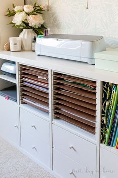 a white shelf filled with lots of books and papers next to a vase full of flowers