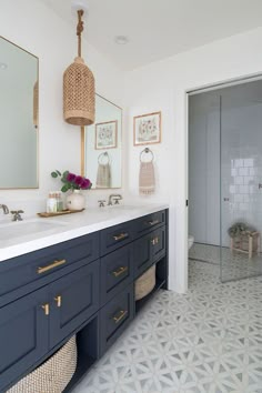 a bathroom with blue cabinets and white tile flooring, two mirrors on the wall