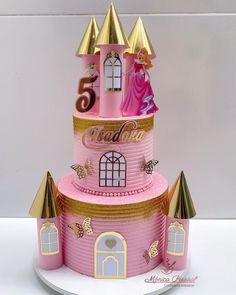 a pink castle cake with gold trimmings and princess figurines on top