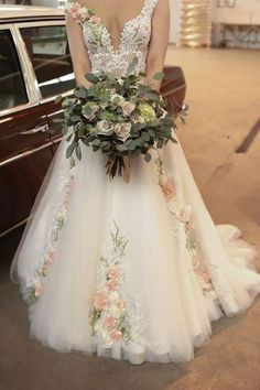 a woman standing next to a car wearing a wedding dress with flowers on the skirt