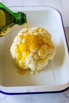 cauliflower being drizzled with honey on a white plate next to a green bottle