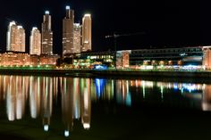 the city is lit up at night and reflecting in the water