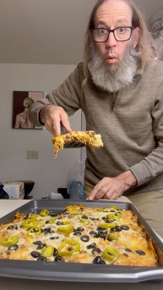 a man with a beard and glasses is holding a piece of pizza in front of him