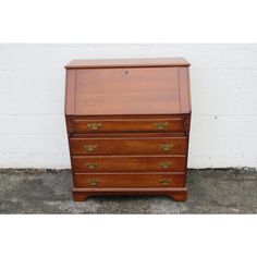 an old wooden chest of drawers with brass hardware on the top and bottom, against a white brick wall