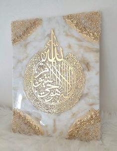 a white and gold wall hanging with an arabic calligraphy in the middle on it