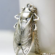 a silver insect necklace sitting on top of a white cup next to a chain bracelet