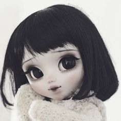 a doll with black hair and big eyes wearing a white scarf around her neck,