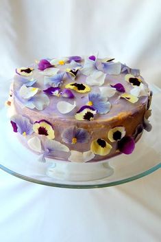 a cake with purple and yellow flowers on top is sitting on a glass platter