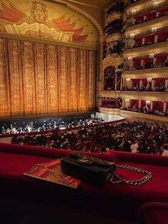 an auditorium filled with lots of people sitting on red couches next to a stage