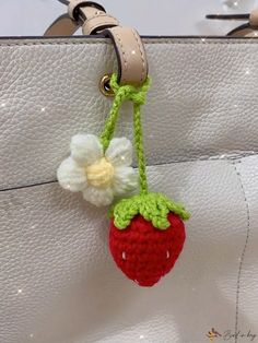 a small crocheted strawberry hanging from a white purse with a flower on it