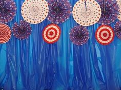 several patriotic paper fans are hanging on a blue curtain with red, white and blue decorations