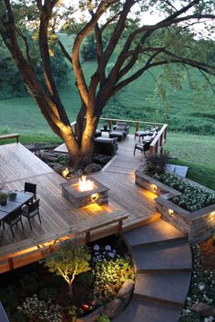 an outdoor deck lit up with lights and seating under a tree in the middle of a yard