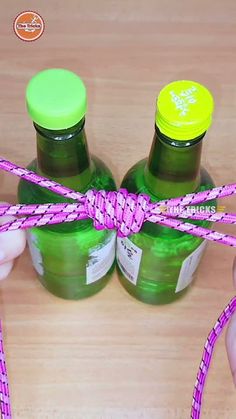 two green bottles tied with pink and yellow twine on top of a wooden table