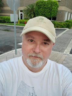 a man with a white beard wearing a hat and looking at the camera while standing in front of a stop sign